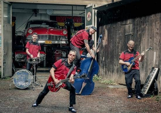 Die BlueShows Band mit Instrumenten vor der Garage, im Hintergrund ein roter Oltimer auf dem Lift